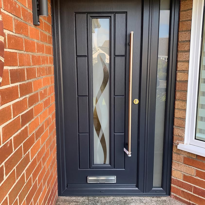 Dark entrance door with a tall decorative glass panel beside a brick wall